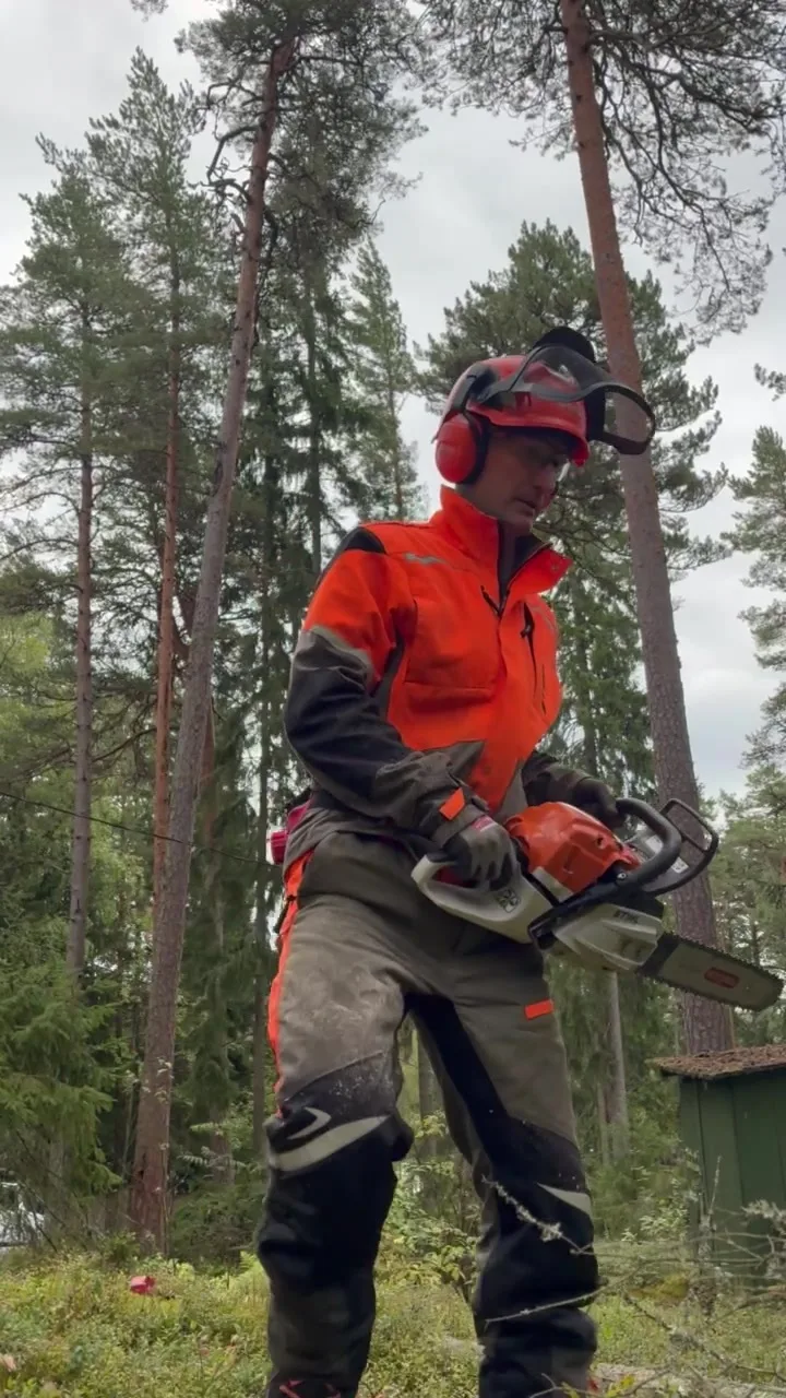 Metsuri kävelee metsässä täydessä turvavarustuksessa moottorisaha kädessä